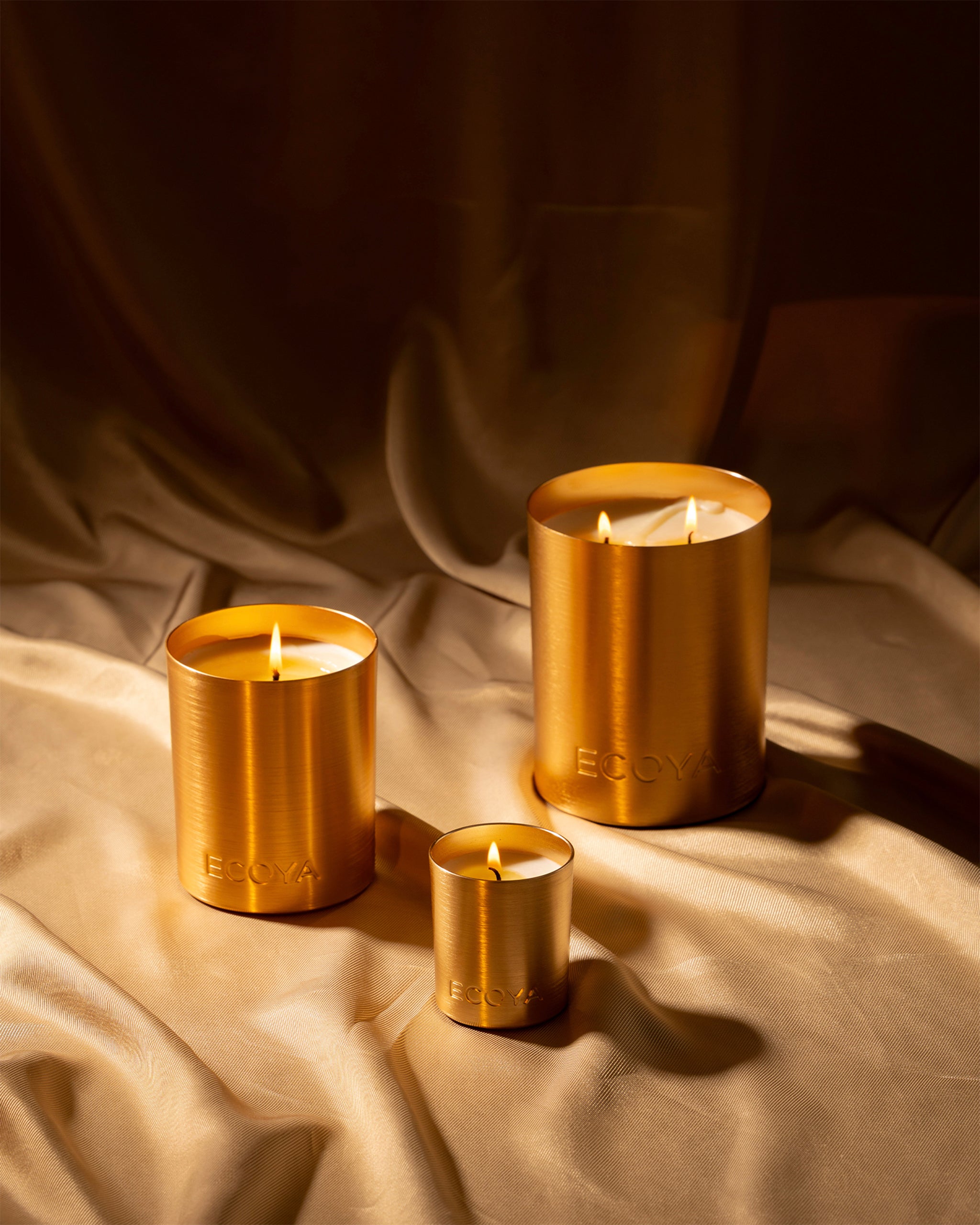 Three pine fragranced gold candles with 'ECOYA' branding on a textured fabric background