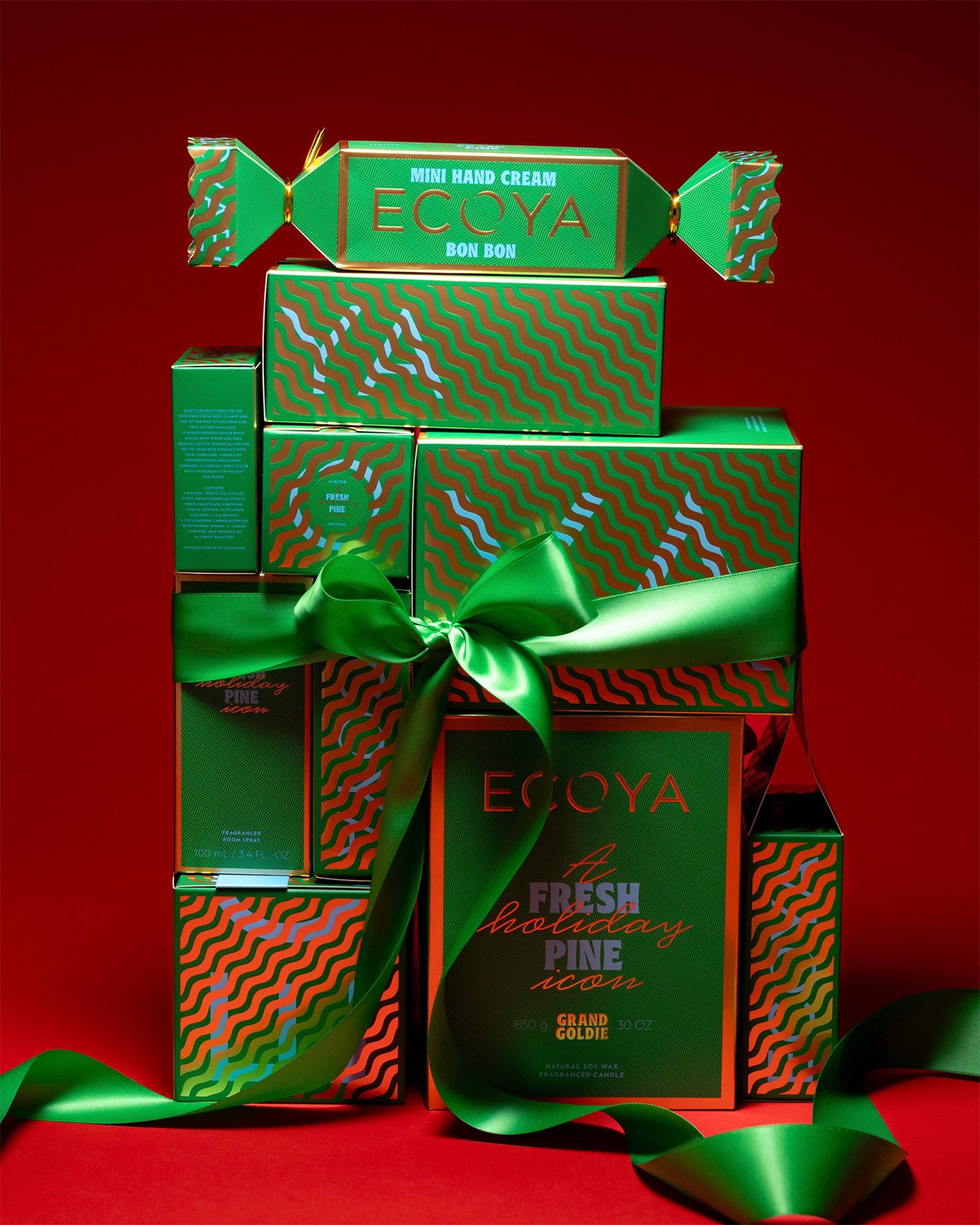 Stack of green 'ECOYA' christmas gift boxes with a decorative bow on a red background